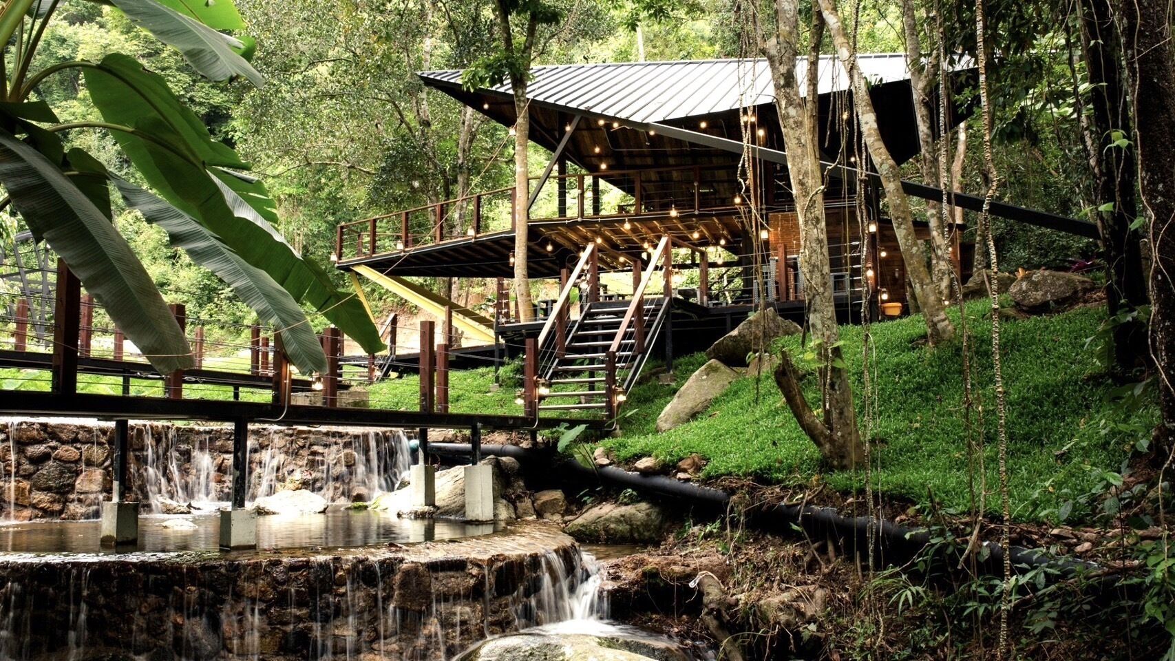 Ein rustikales Holzgebäude mit einem Metalldach, einem kleinen Wasserfall und einer Brücke dorthin.