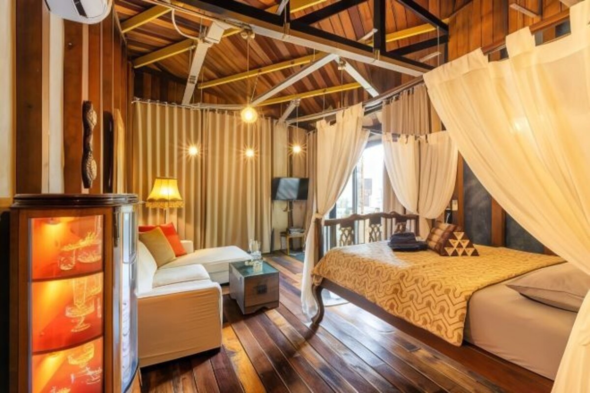 Una habitación acogedora con techo de madera, cama con colcha estampada, sofá con cojines, una mesita y un televisor.