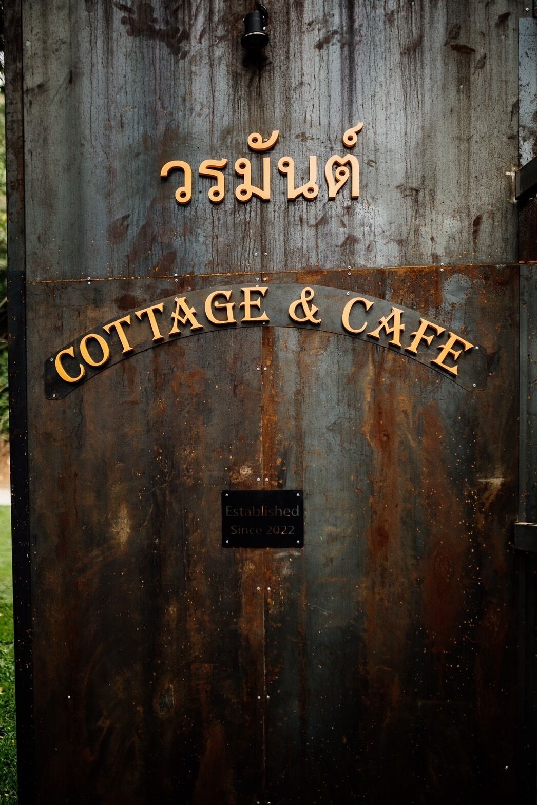 Una reja metálica rústica con la inscripción "COTTAGE & CAFE" y un cartel que dice "Establecido desde 2022".