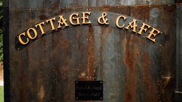Una reja metálica rústica con la inscripción "COTTAGE & CAFE" y un cartel que dice "Establecido desde 2022".