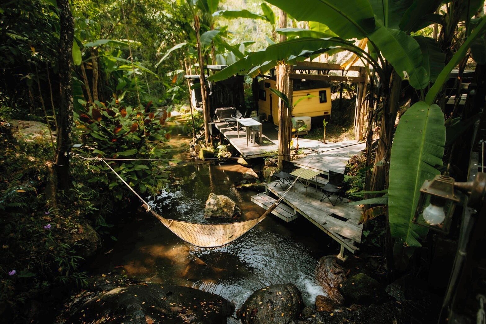 A rustic wooden bridge over a stream, a hammock, and a small wooden structure with a yellow exterior.