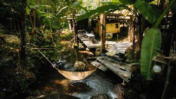 A rustic wooden bridge over a stream, a hammock, and a small wooden structure with a yellow exterior.