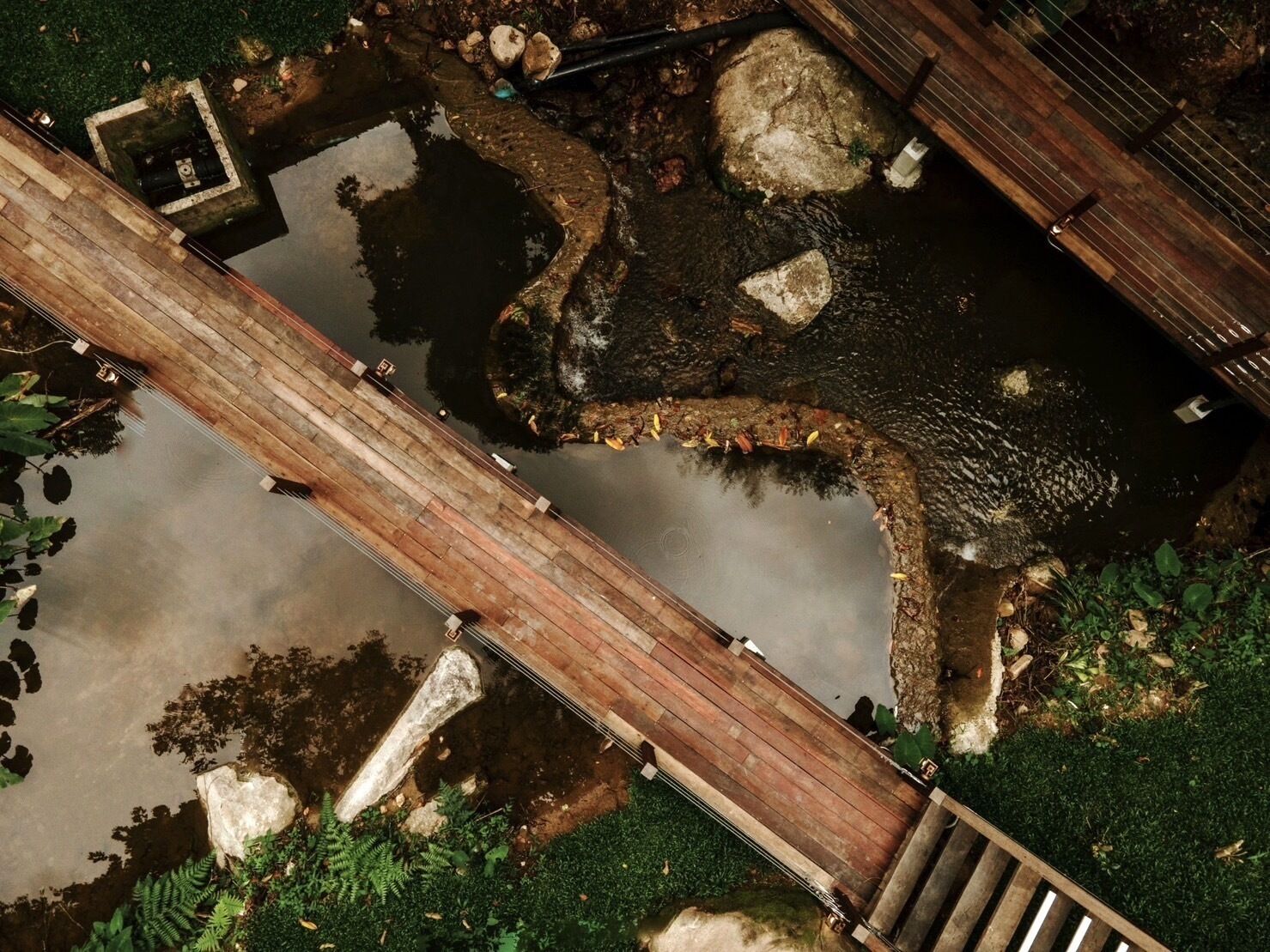 Un puente de madera sobre un estanque con rocas y follaje circundante.