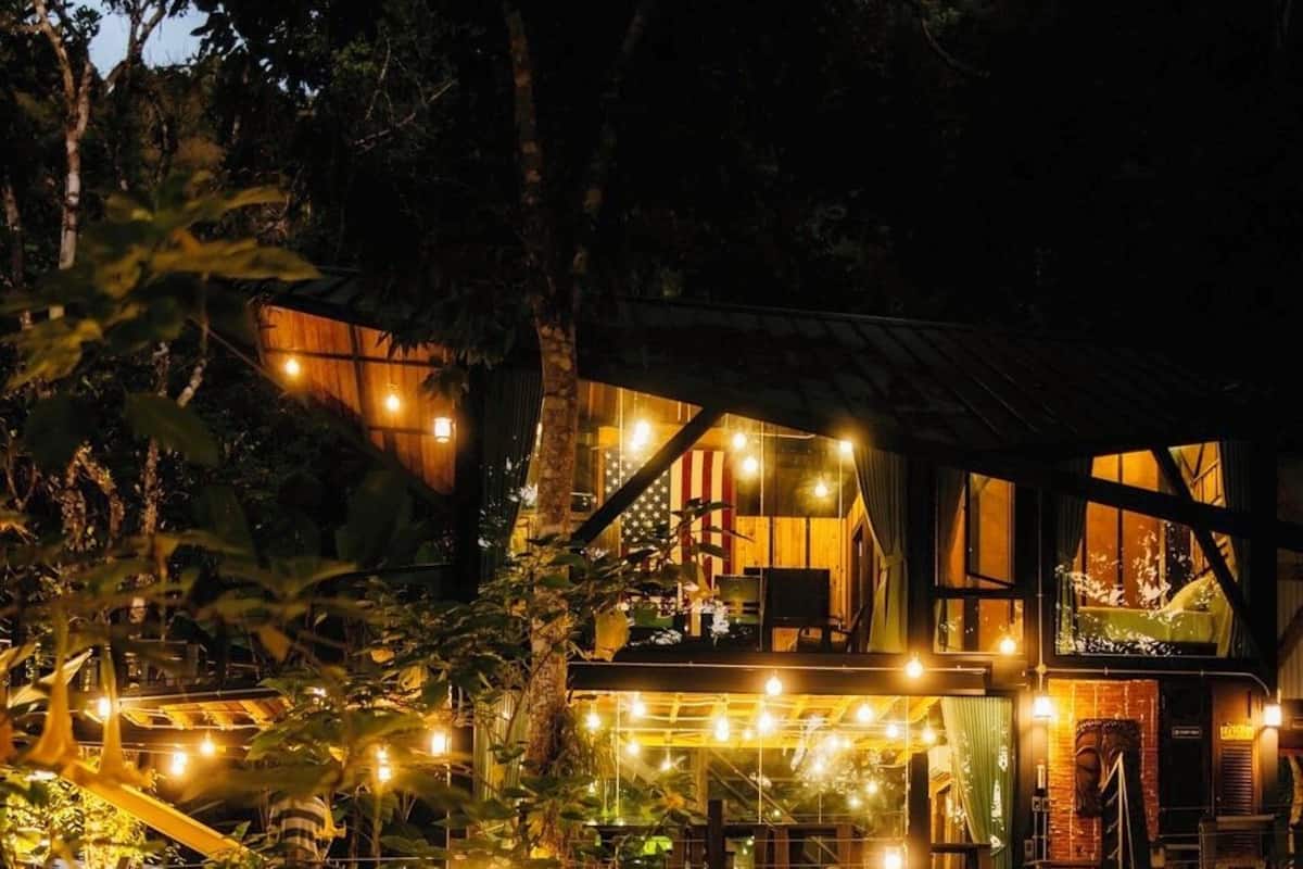 Una terraza de madera que conduce a un edificio con guirnaldas de luces y una cascada.