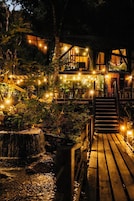 Una terraza de madera que conduce a un edificio con guirnaldas de luces y una cascada.