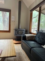 Un salón acogedor con chimenea, un sofá, una mesa y ventanas amplias.