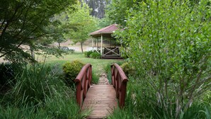 A wooden bridge leading to a gazebo in a lush garden.