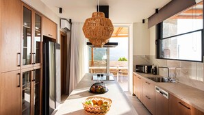 Una cucina moderna con mobili in legno, un'isola centrale con un cesto di frutta, una grande finestra e vista sul mare.
