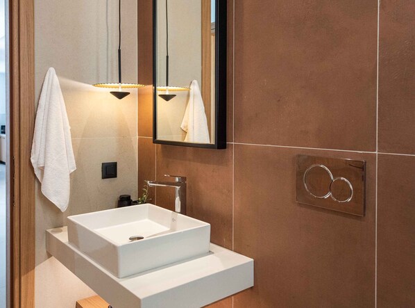 A modern bathroom with a white sink, a mirror, and a towel hanging on the wall.