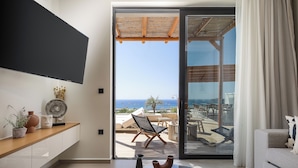 Una sala de estar moderna con un televisor grande, una consola de madera con objetos decorativos, un sofá y vistas al océano a través de un ventanal corredero.