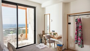 Un dormitorio con una cama grande, un escritorio y una silla. Hay un balcón con vista al mar.