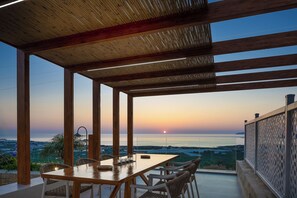 An outdoor dining area with a view of the sunset over the sea, wooden beams, and a table with chairs. - Villa Domenica Free* heated pool & Seaviews (Kissamos)