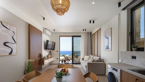 Una cocina moderna con lavadora incorporada, un comedor con mesa y sillas de madera, y vista al mar a través de un ventanal corredero.