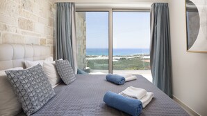 A bedroom with a large bed, a stone wall, and a view of the sea. - Villa Elpida Sea view & heated* pool! (Kissamos)