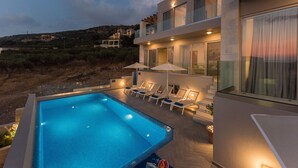 A modern poolside area with a rectangular pool, lounge chairs, and umbrellas.