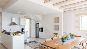 A modern kitchen with white cabinets, a built-in island, and a dining area with a wooden table and chairs. - Villa Galatia I Free*heated pool, ideal for groups (Kissamos)