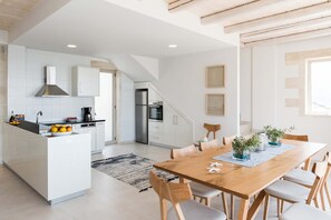 A modern kitchen with white cabinets, a built-in island, and a dining area with a wooden table and chairs. - Villa Galatia I Free*heated pool, ideal for groups (Kissamos)
