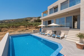 A modern pool area with a clear blue pool, sun loungers, and a view of the surrounding landscape.