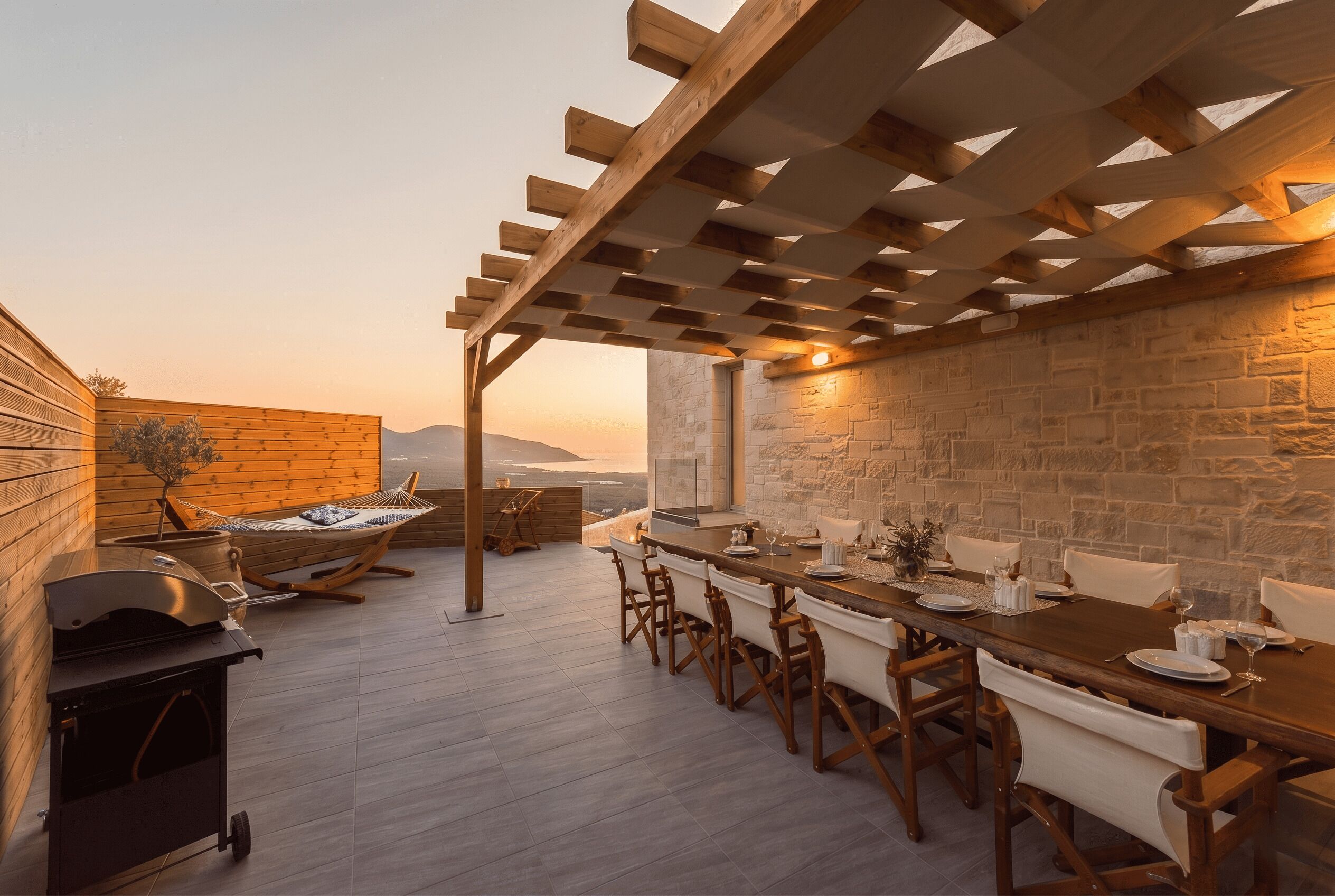 An outdoor dining area with a pergola, stone wall, and a view of the landscape.