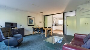 Una sala de estar moderna con una mesa de centro de vidrio, un sofá de cuero rojo, un comedor con una mesa y sillas de madera, un televisor y un cuadro en la pared.