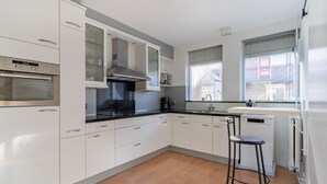 Una cocina moderna con armarios blancos, un horno de acero inoxidable, una encimera negra y un taburete de bar.
