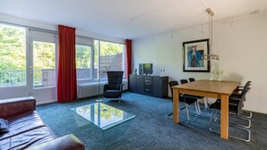 Una habitación moderna con una mesa de centro de vidrio, un sofá, una mesa de comedor con sillas, un televisor y un radiador.