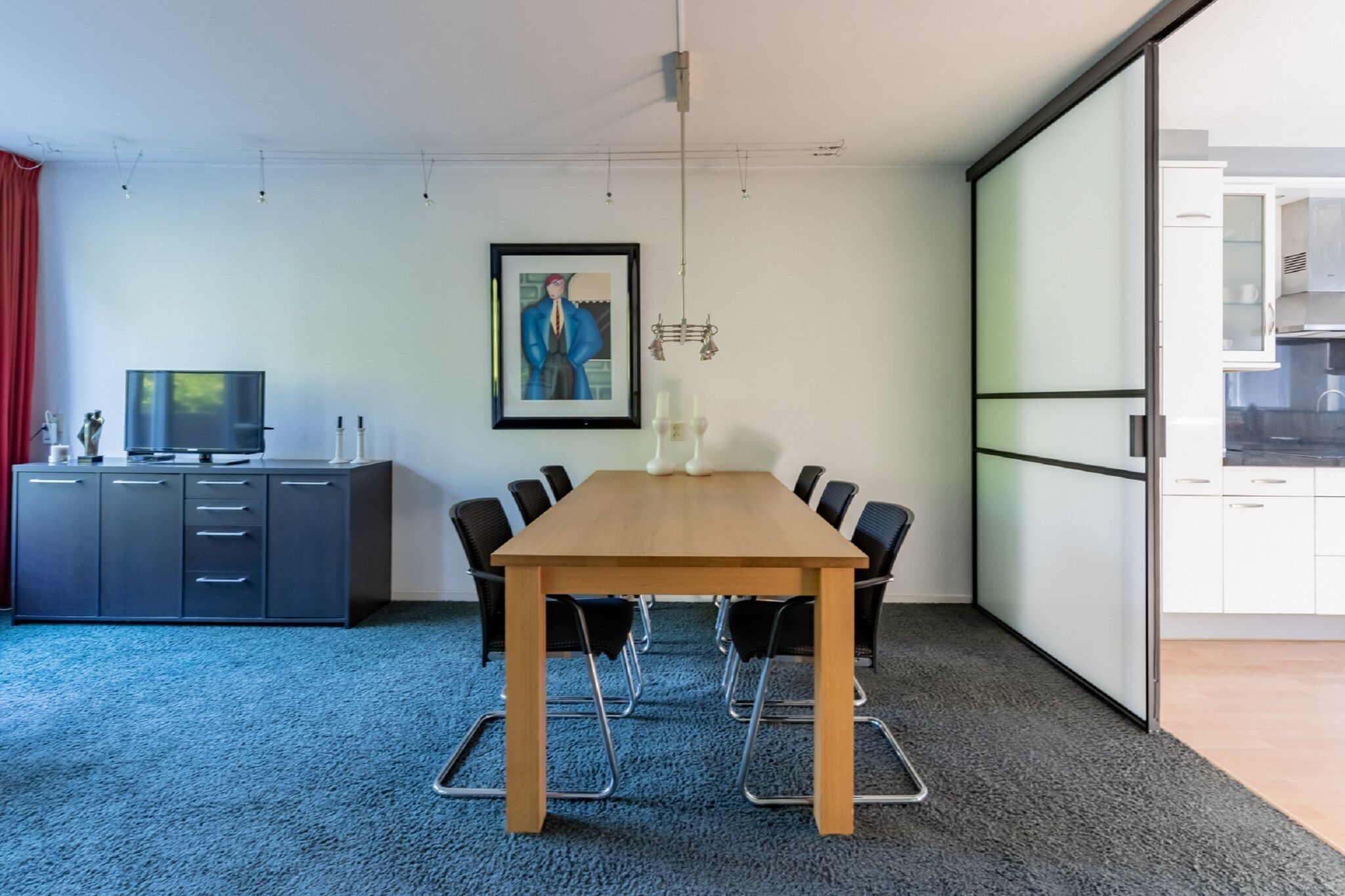 A conference room with a long table, black chairs, a grey cabinet, and a framed picture on the wall.