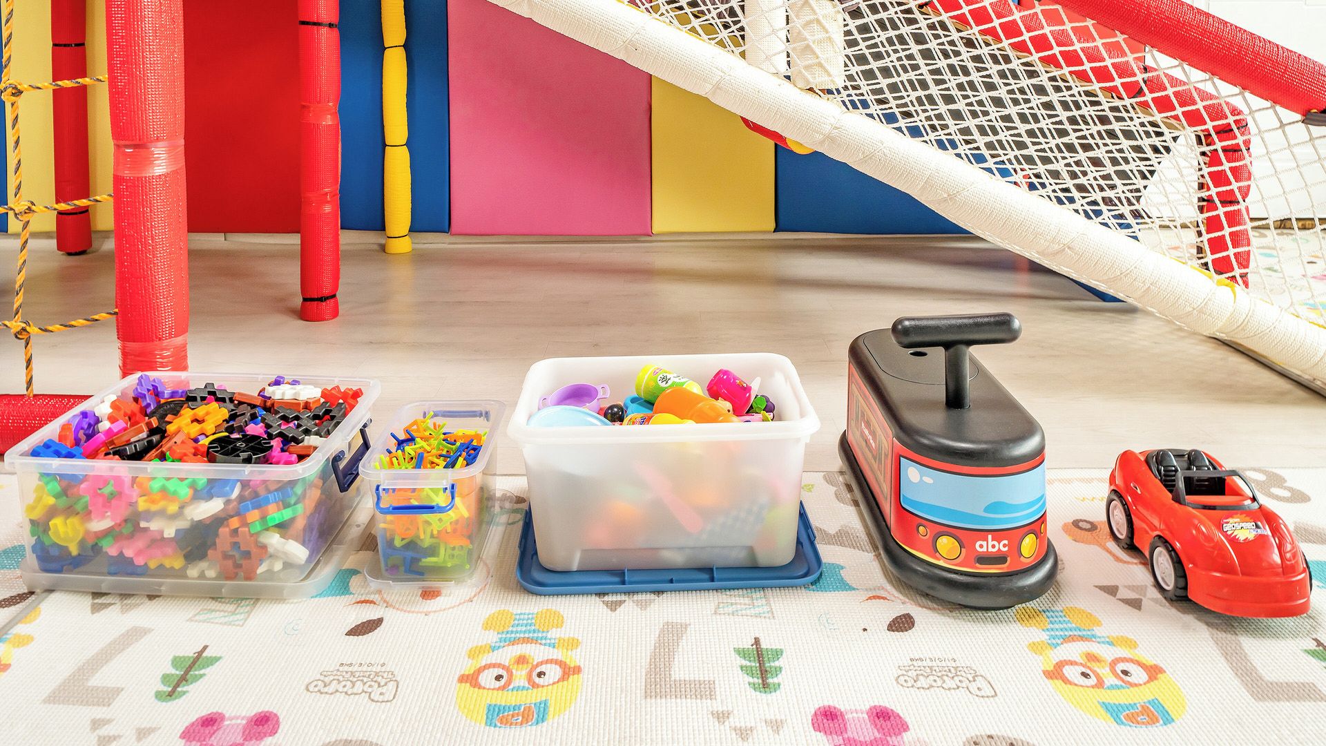 A play area with a netted soccer goal, colorful play structures, and various toys including a toy car and a toy train.