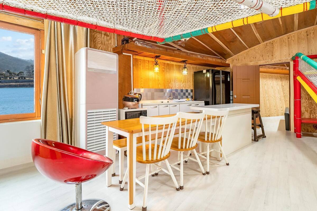 A cozy kitchen with a view of the water, wooden cabinets, a red chair, and a dining table.