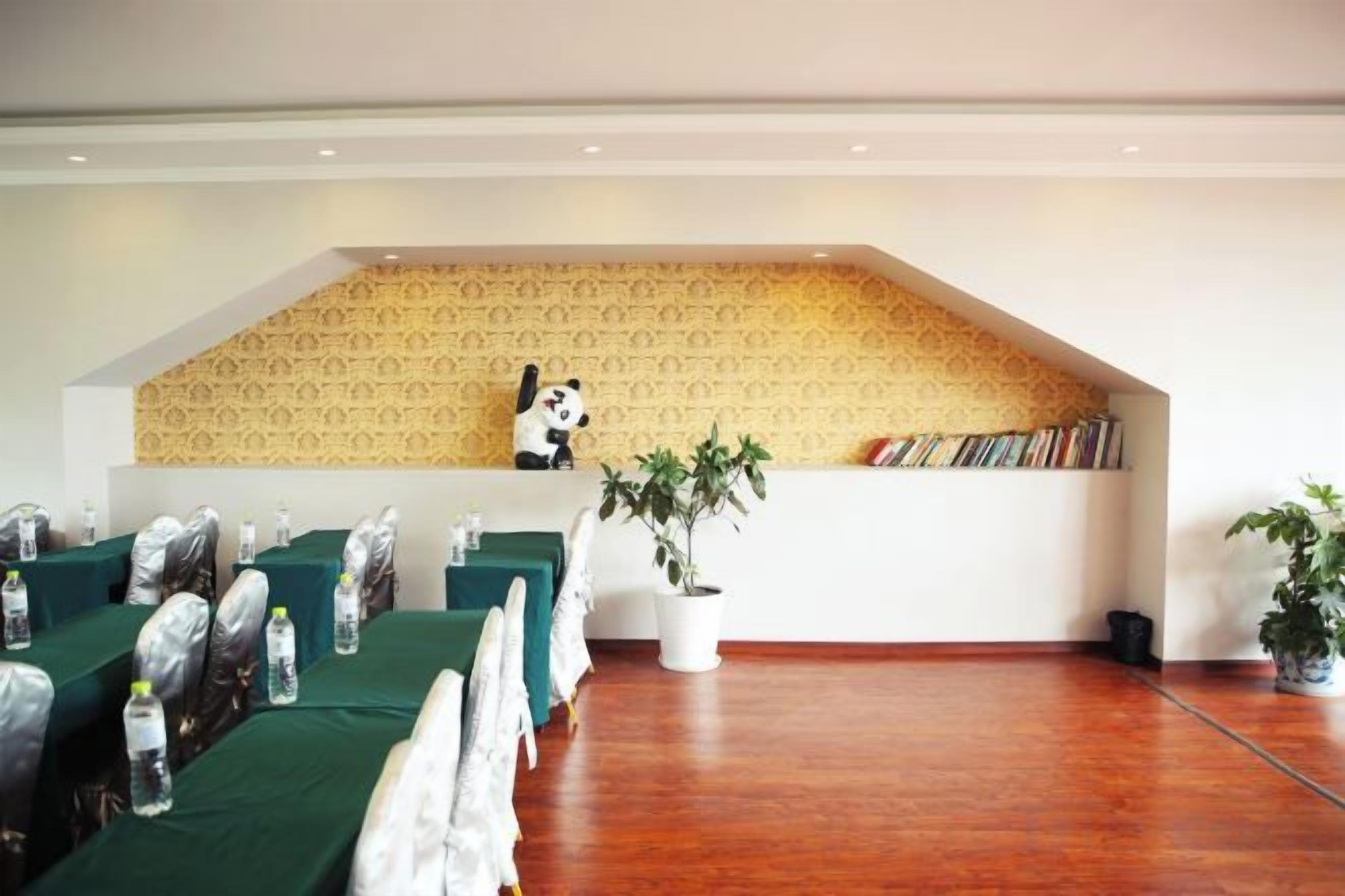 A conference room with tables set up for a meeting, a bookshelf with books, and a panda statue on a shelf.