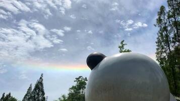 Een grote bolvormige sculptuur met een kleinere bol bovenop, voor een achtergrond van een bewolkte lucht en een regenboog.