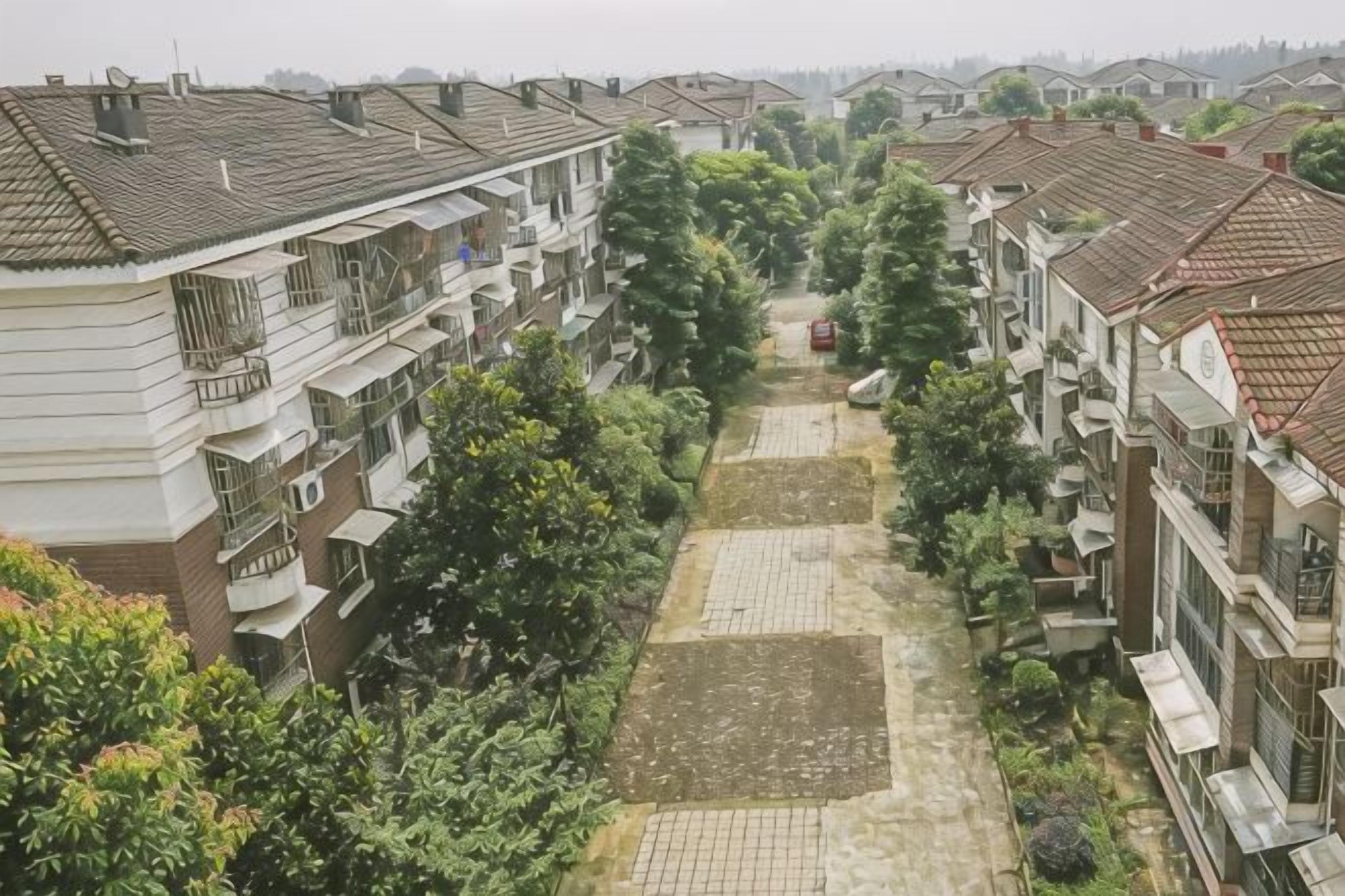 A residential area with multi-story buildings, a paved pathway, and greenery.