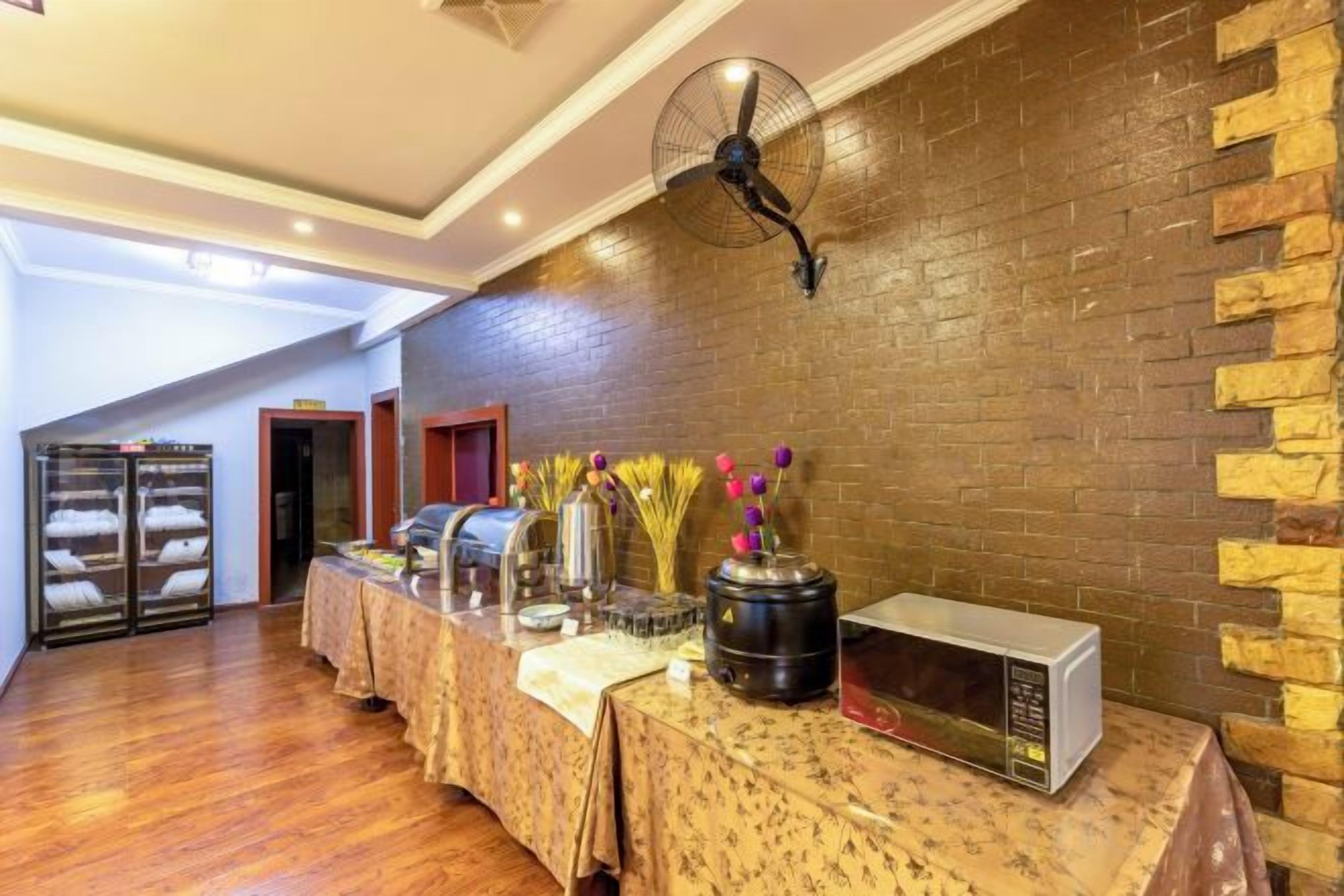 Quarto com uma mesa comprida, um ventilador, micro-ondas e parede de tijolos.