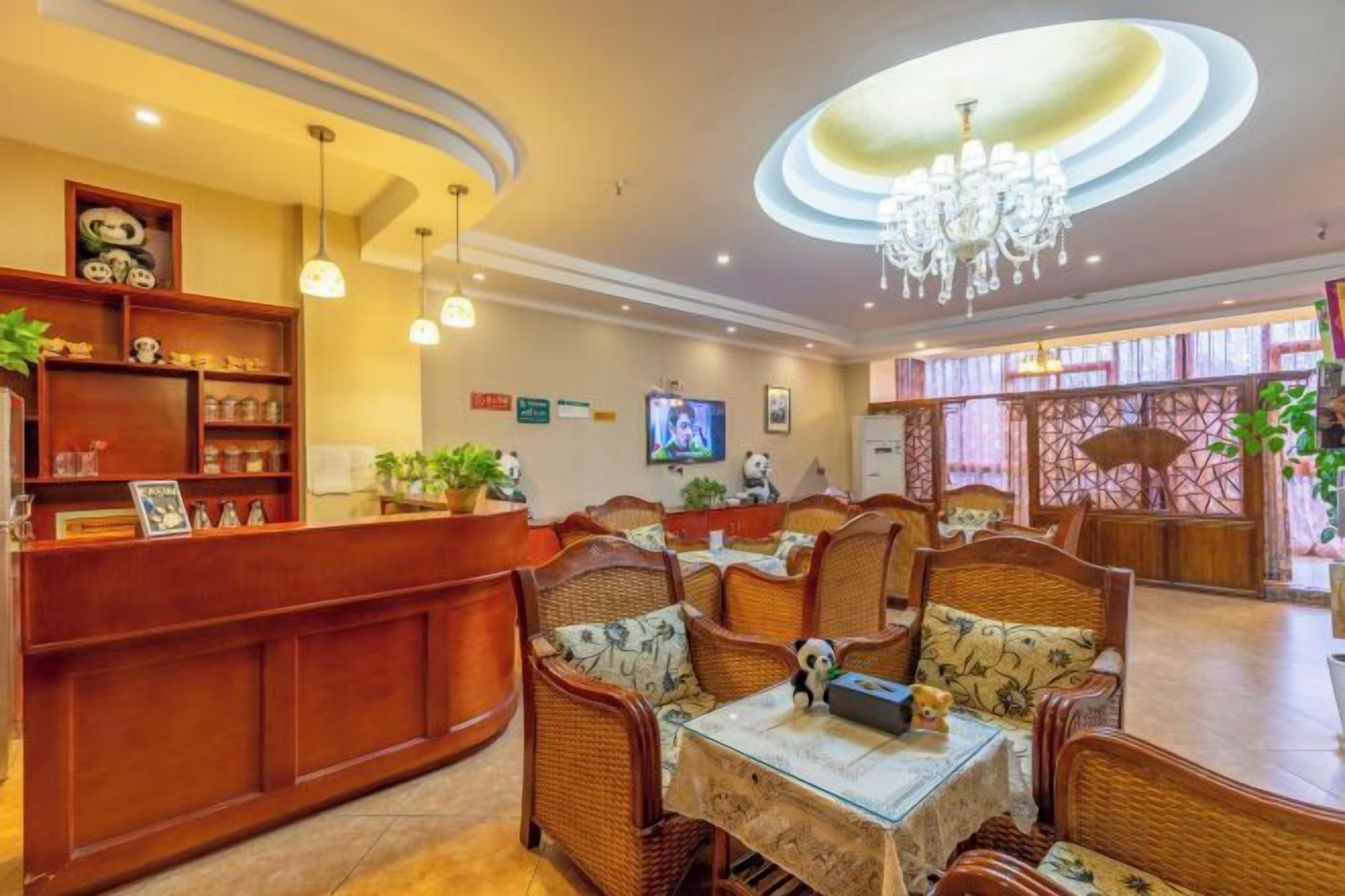 A hotel lobby with a reception desk, wicker furniture, a chandelier, and a television on the wall.
