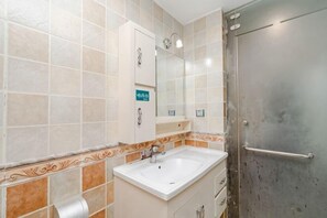 Un baño con lavabo, espejo, dispensador de toallas y mampara de ducha.