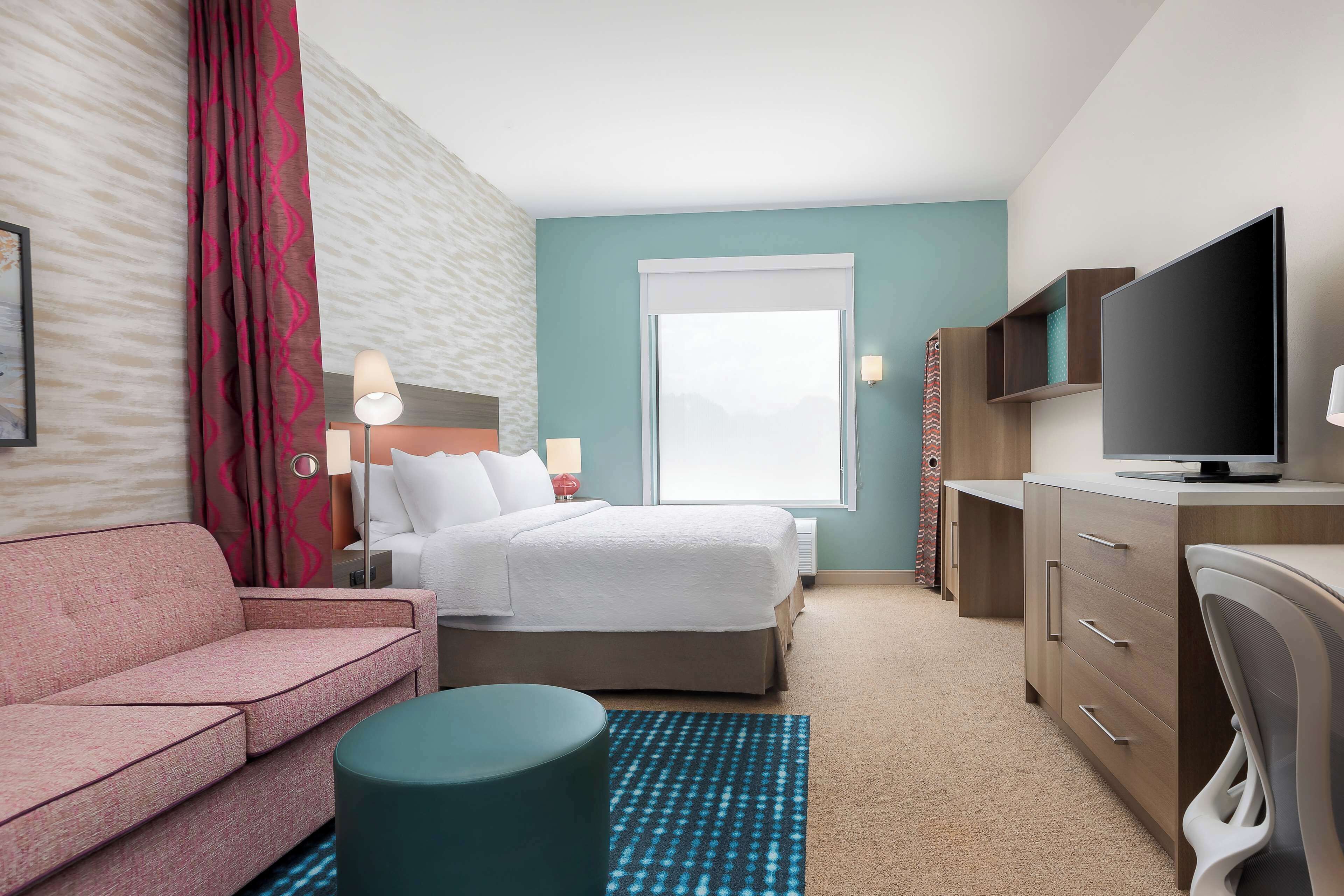 Een hotelkamer met een bed, een bank, een bureau met een televisie, een lamp en een raam met uitzicht.
