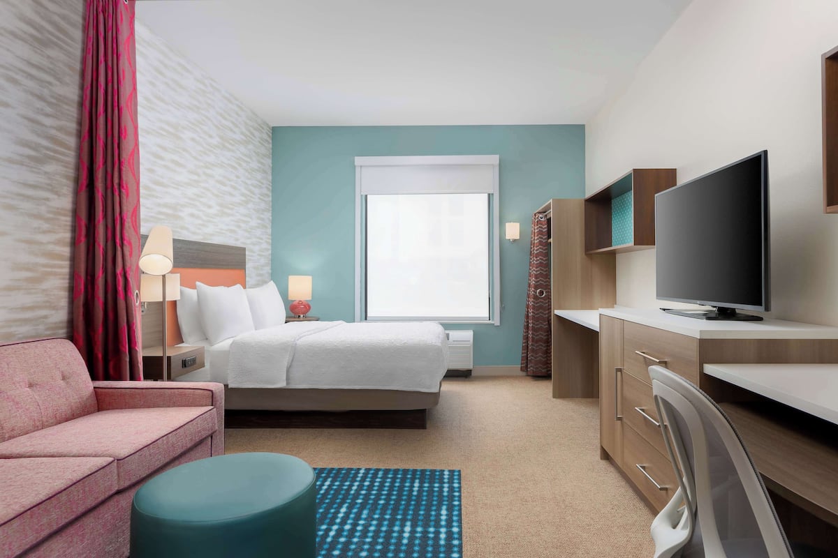 A hotel room with a bed, a desk, a TV, a sofa, and a window with curtains.
