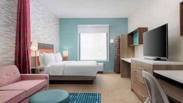 A hotel room with a bed, a desk, a TV, a sofa, and a window with curtains.