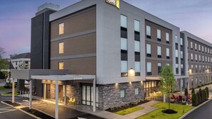 Il s'agit d'un hôtel moderne, reconnaissable à son enseigne « HOME 2 Suites by Hilton ». Le bâtiment présente une architecture à plusieurs étages, avec une façade combinant briques et verre, des espaces de détente en plein air et un parking agrémenté de flèches directionnelles.
