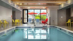 Une piscine dont le bord est recouvert de carreaux, des chaises jaunes et rouges, et une vue sur les arbres à travers les portes vitrées.