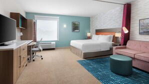 Une chambre d’hôtel comprenant un lit, un bureau avec une chaise, une télévision, un canapé et un tapis à motifs.