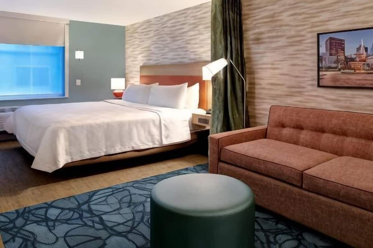 A hotel room with a bed, a sofa, a small table, and a cityscape painting on the wall.
