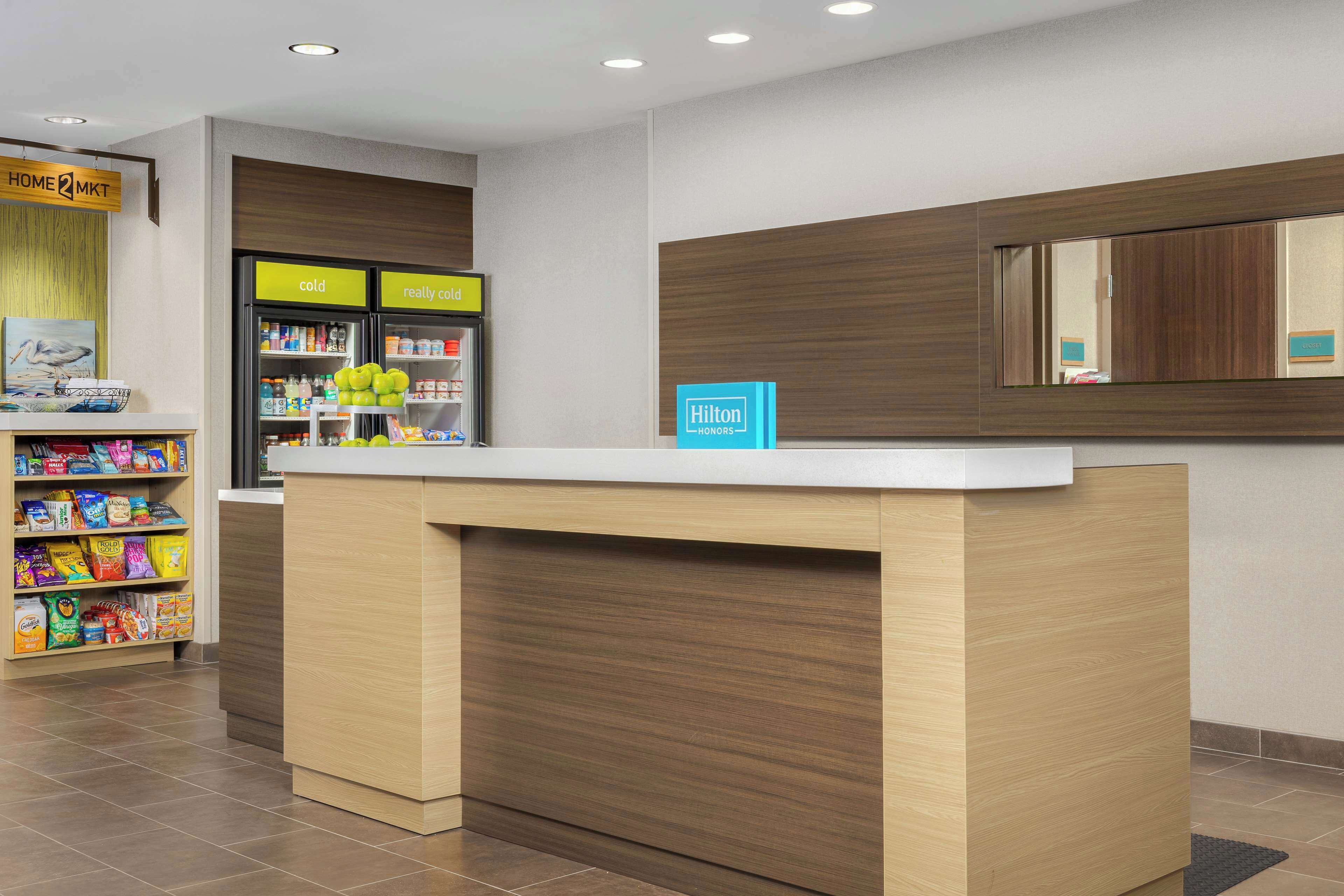 Zona de recepción de hotel con mostrador de madera, minibar y máquina expendedora de bebidas.