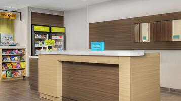 Zona de recepción de hotel con mostrador de madera, minibar y máquina expendedora de bebidas.