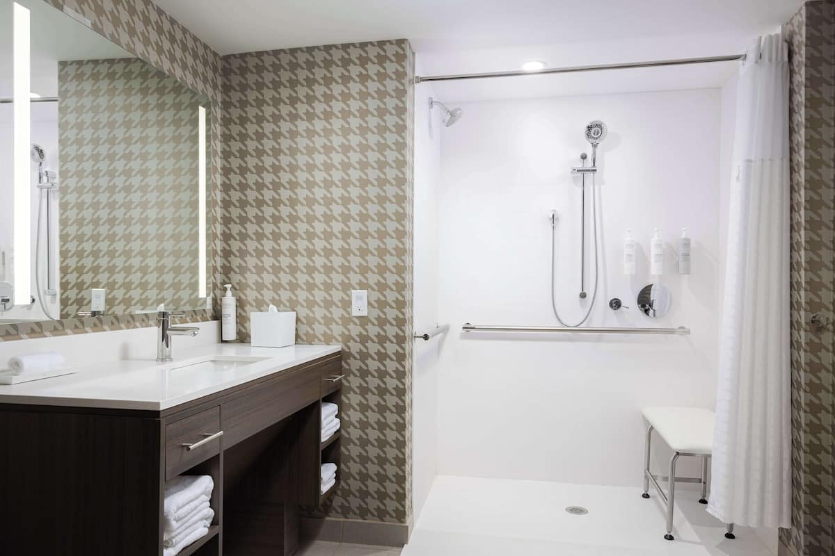 A modern bathroom with a dual sink vanity, a walk-in shower, and a small stool.