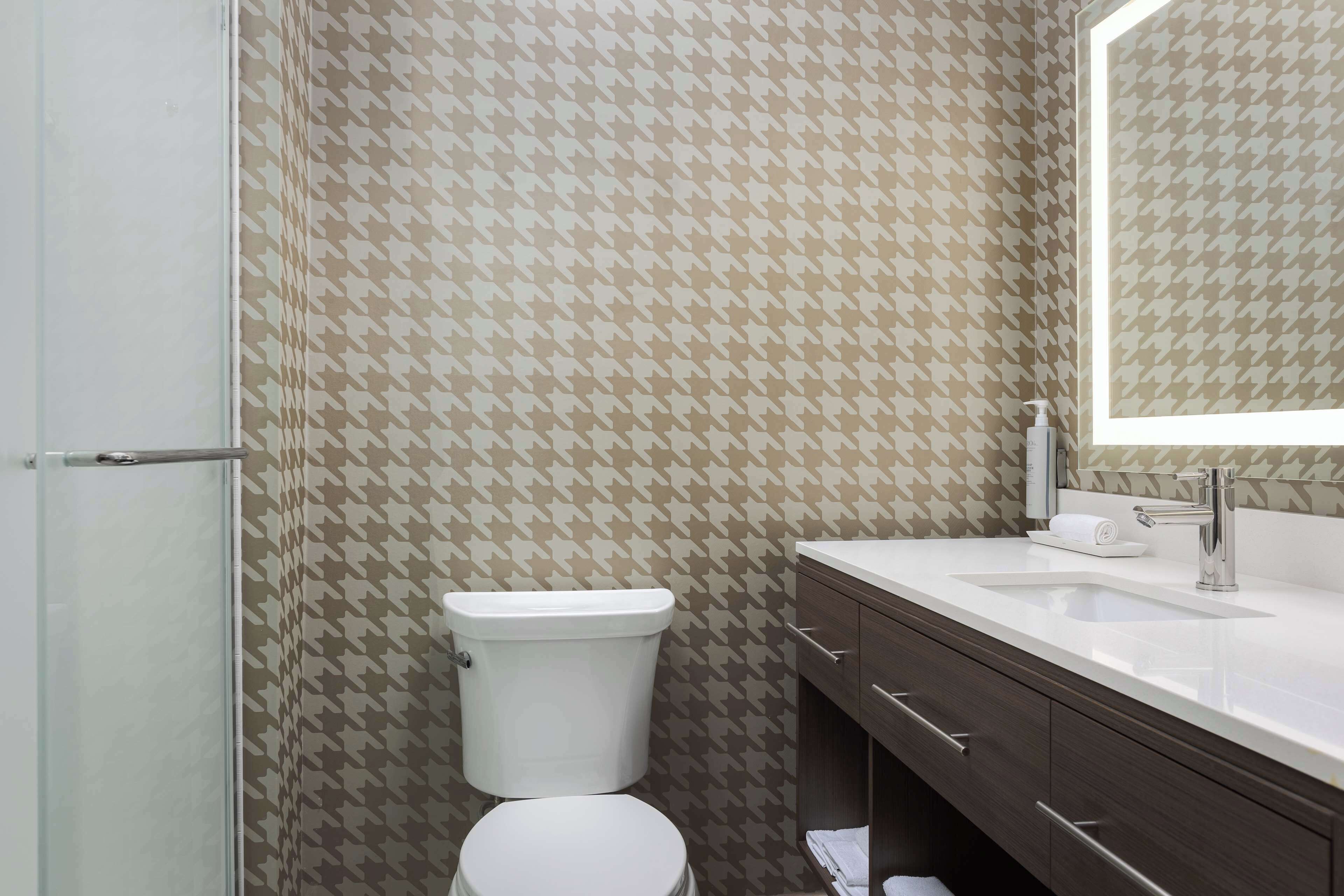 A bathroom with a patterned wall, a toilet, a sink, and a mirror.
