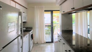 Una cocina estrecha con armarios blancos, un refrigerador y un microondas. Hay una puerta corrediza de vidrio que da a un área exterior con una mesa y sillas.