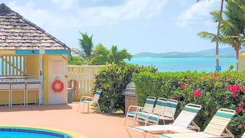 A pool area with lounge chairs, a lifebuoy, and a building with a tiled roof.