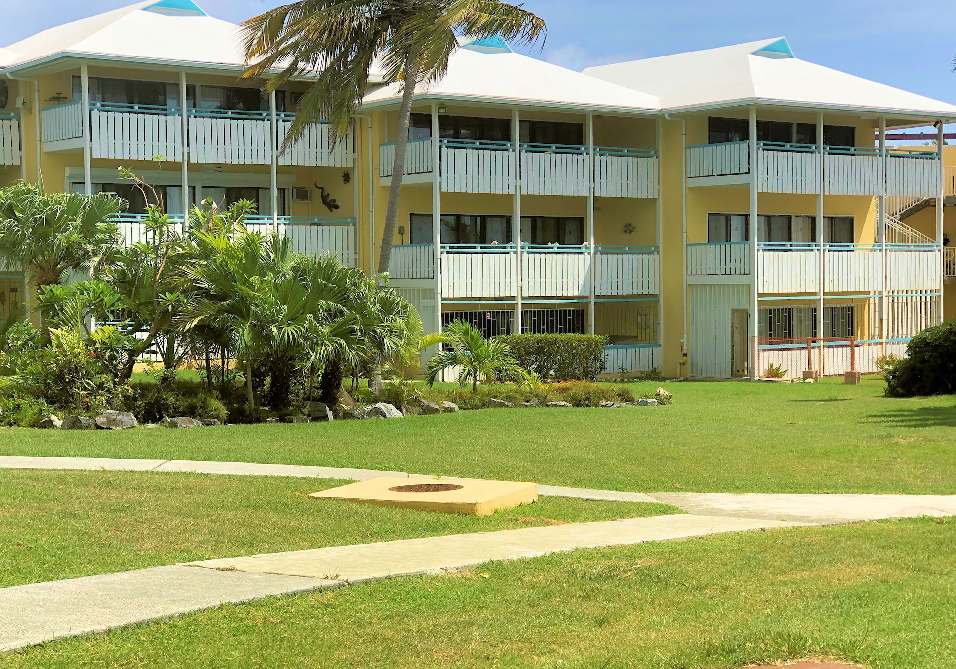 A multi-story hotel with balconies, a well-maintained lawn, and a palm tree.