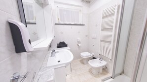 Une salle de bain moderne équipée d’un lavabo, de toilettes, d’un bidet et d’une douche séparée par une paroi de verre.